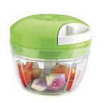 Compact manual pull-string food chopper with a bright green lid and clear bowl, filled with freshly chopped tomatoes, onions, and mixed vegetables, shown on a white background.
